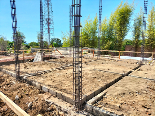 Construction project, sloof and coloumn reinforcing bar during time construction period. Building foundation construction site with concrete footing and steel reinforcement structure. Construction site showing building foundation work with concrete footing and vertical steel reinforcement bars. Early stage of building construction, suitable for engineering, architecture, civil construction, infrastructure development, and industrial project concept.