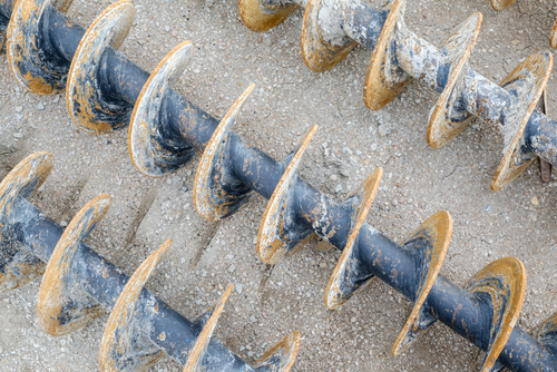 Rusted steel auger drill bits for soil boring and geotechnical ground testing at a construction site.