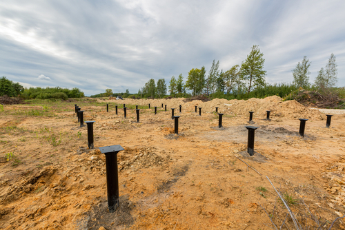 Iron screw pile foundation installation at a construction site for new building construction on sandy terrain