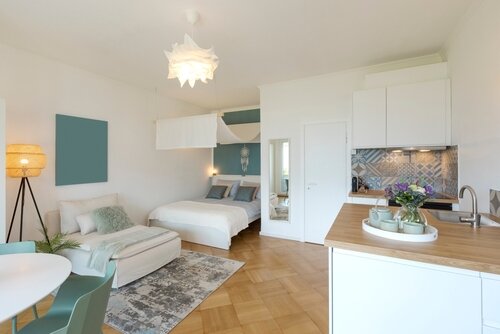 General view of a stylish modern studio apartment. There is a small kitchen with a wooden counter, a double bed and a single bed, and a table with chairs. No one inside