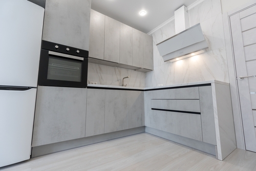 Modern L-shaped kitchen with grey cabinets, built-in oven, chimney, and marble wall panels