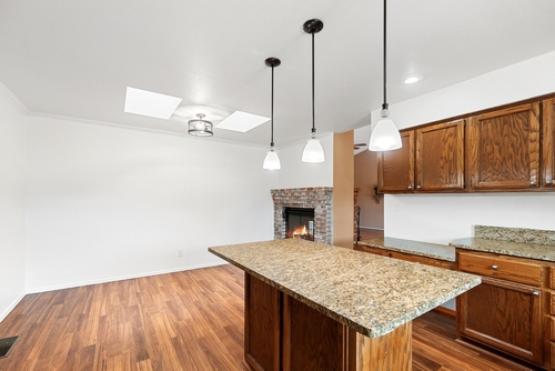 Home kitchen with wood cabinets, granite island countertop, pendant lights, and fireplace