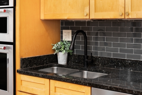 Kitchen with wood cabinets, black subway tile backsplash, granite countertop, and double sink