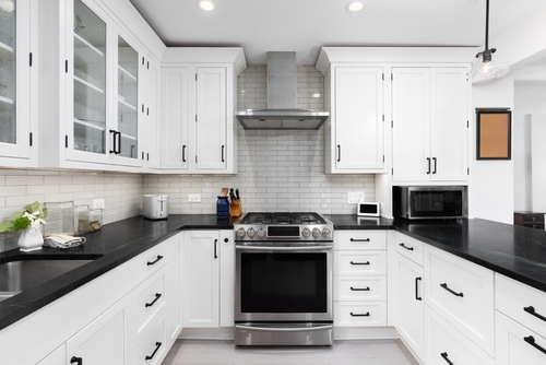 Modern kitchen with white cabinets, subway tile backsplash, black countertops, and gas stove