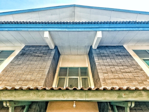 Symmetrical upward view of building facade with textured masonry columns, teal roofline and central window — architectural detail and perspective.