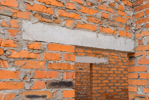 Exposed brick wall with cement lintel above a doorway in an unfinished building.
