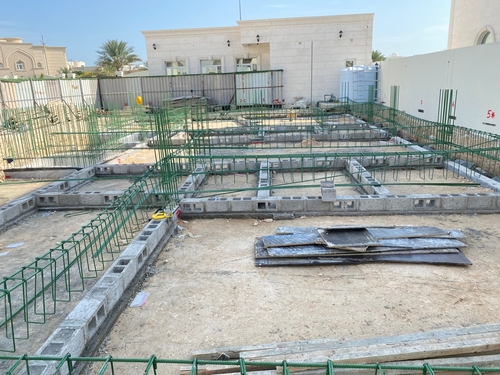 Construction site showing green rebar cages and concrete blocks for a building foundation