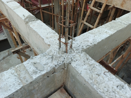 Close-up of a concrete beam intersection with exposed vertical rebar and scaffolding