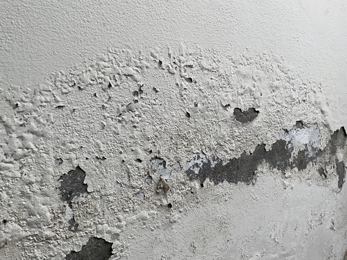 Damaged concrete wall with peeling surface and exposed patches of deteriorated plaster