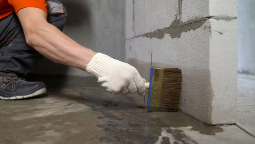 Worker applying waterproofing coating to a concrete wall using a brush