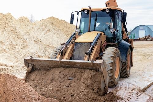 The excavator backfills the pit with the front bucket. Moves soil around the construction site. Close-up. Heavy construction equipment