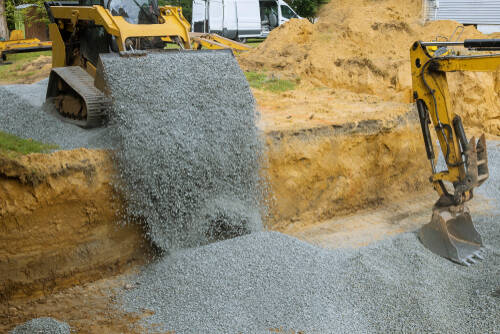 Excavator bucket backfilling trench for stone backfill of foundation excavator bucket working