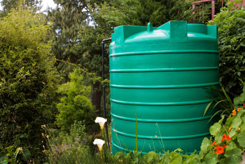 Green water tank in a garden setting with flowers in the foreground