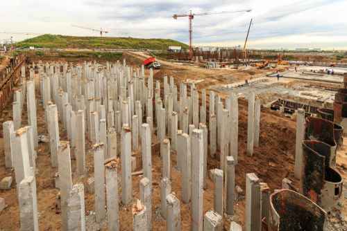Construction site par zameen me gade cement ke pillars aur crane