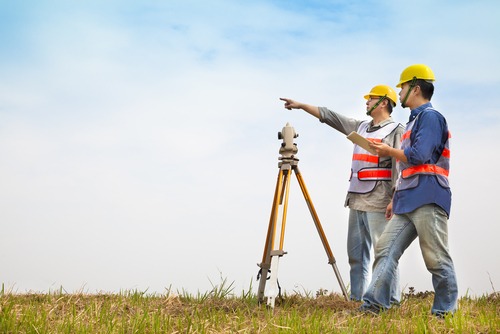 Maidaan mein survey instrument ke paas khade do engineers