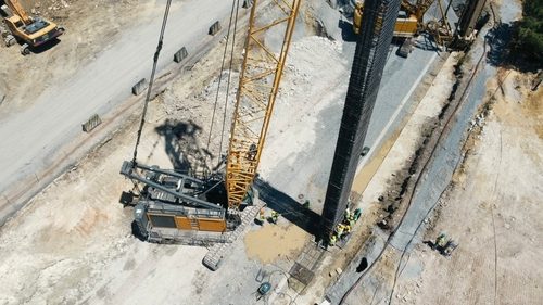Crane aur workers deep foundation ke liye lohe ka cage set karte hue