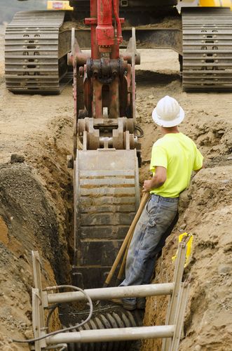 Mitti ka gaddha khodne ke dauran excavator machine ke paas khada ek construction worker