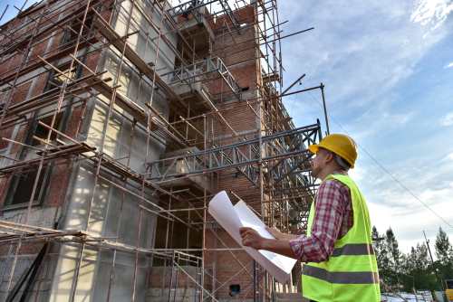 Ban rahi building ke samne haath me naksha liye khada site engineer