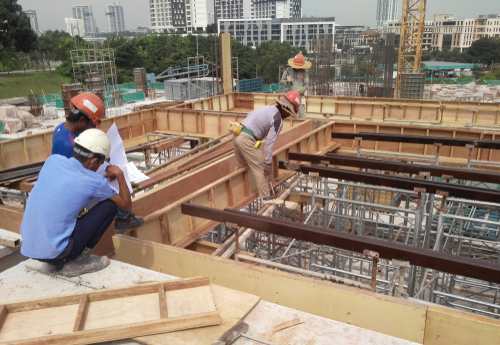 Construction site par dhalai ke frame ke paas naksha dekhte workers
