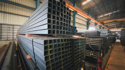 Industrial warehouse me ek ke upar ek rakhe hue heavy square steel pipes