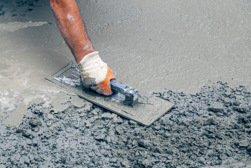 Hand builder with trowel leveling concrete, spreading poured. Some motion blur present. Vintage style.