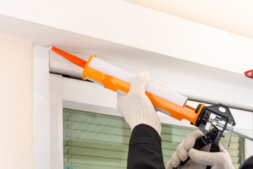 Technician man hand holding and using glue gun, silicone tube or manual caulking gun to seal the expansion joint between cement wall and the metal.