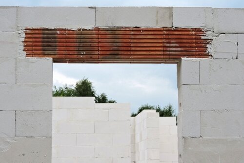 A reinforced brick lintel, a rough door opening and walls made of autoclaved aerated concrete, green trees and blue sky in the background