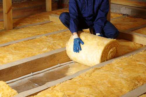 Construction worker thermally insulating house attic with glass wool 