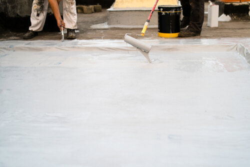 Roof insulation, two man applying material using the paint roller and brush insulating the building