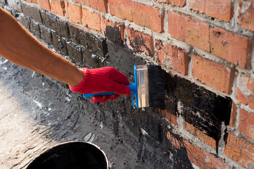 Roofer covered brick wall, bitumen primer for improving adhesion during surfacing, contiguity with rolled waterproofing, during the installation of flat roof.